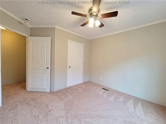 unfurnished bedroom with a textured ceiling, ceiling fan, carpet floors, visible vents, and crown molding