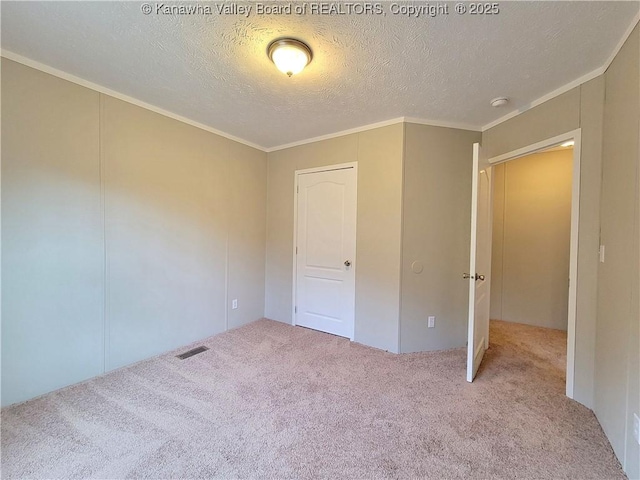 unfurnished bedroom featuring a textured ceiling, ornamental molding, carpet, and visible vents