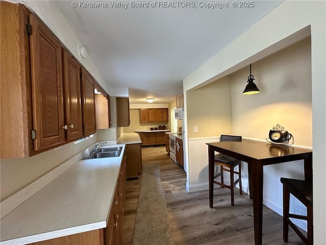 kitchen with white microwave, a sink, wood finished floors, brown cabinets, and electric range oven