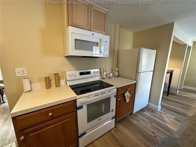 kitchen with light wood-type flooring, white appliances, light countertops, and brown cabinetry