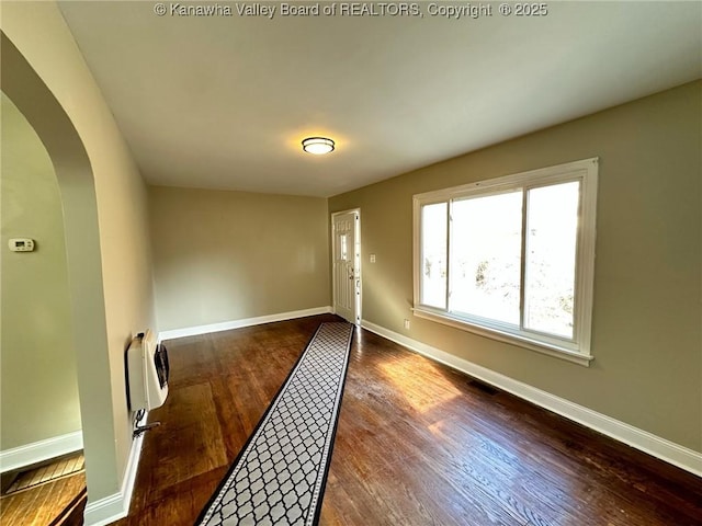 interior space with dark wood-style floors, arched walkways, and baseboards