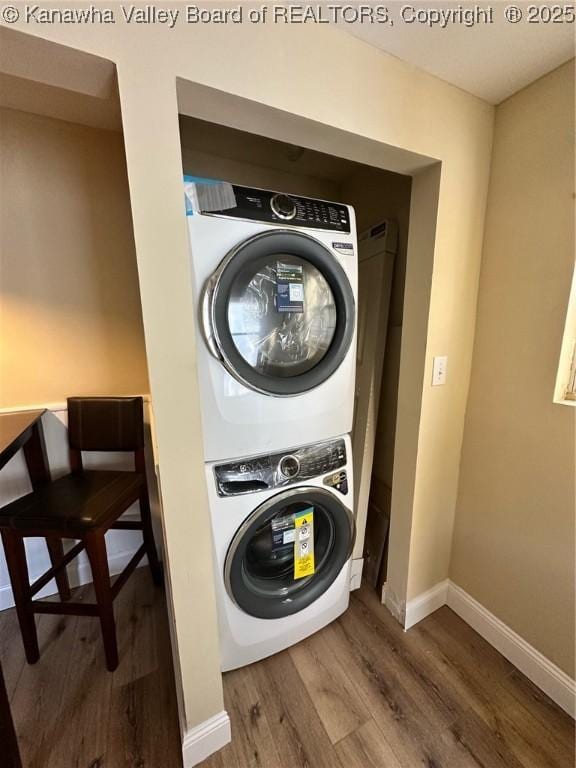 washroom with laundry area, baseboards, stacked washer / dryer, and wood finished floors