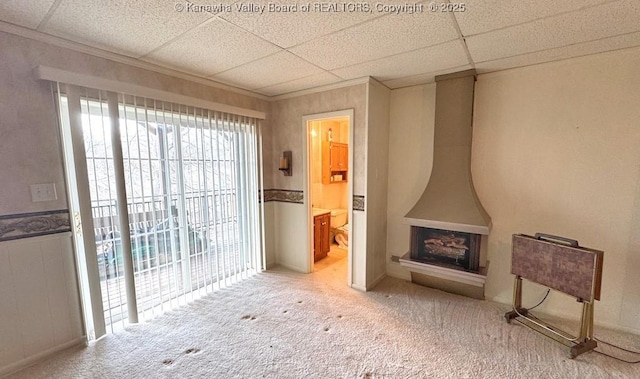 living room with a wood stove, carpet flooring, crown molding, and a drop ceiling