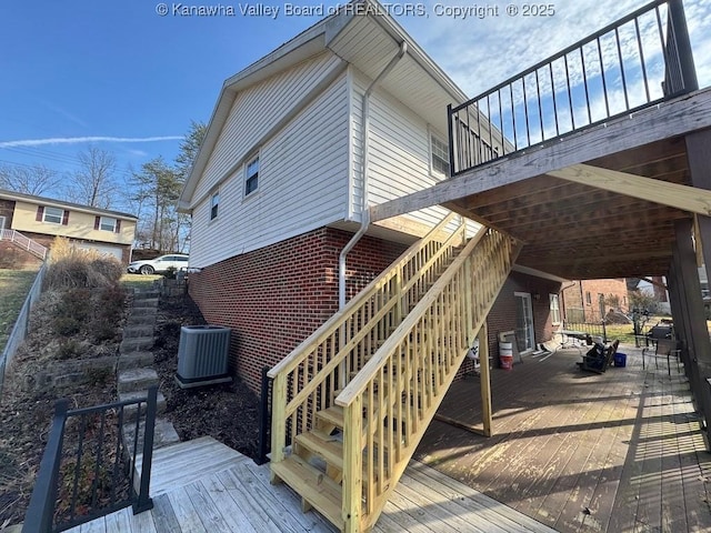 view of side of home featuring central air condition unit, stairway, a deck, and brick siding