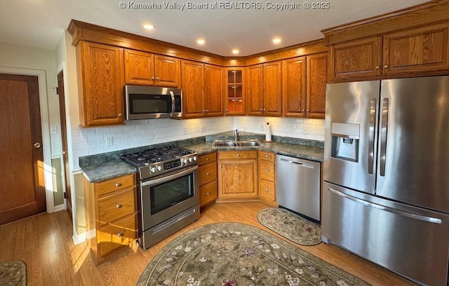 kitchen with appliances with stainless steel finishes, dark countertops, a sink, and light wood-style flooring