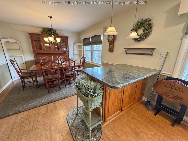 kitchen with a peninsula, light wood-style floors, brown cabinets, dark countertops, and glass insert cabinets