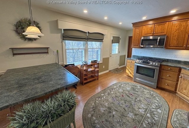 kitchen featuring light wood-style flooring, stainless steel appliances, backsplash, brown cabinets, and dark countertops