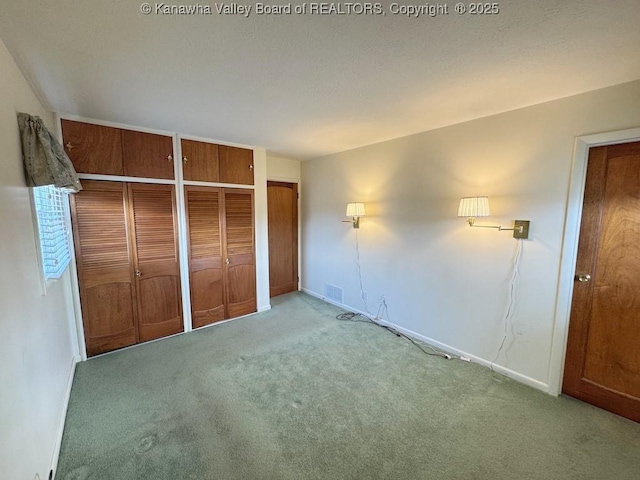 unfurnished bedroom with carpet floors, visible vents, baseboards, and two closets