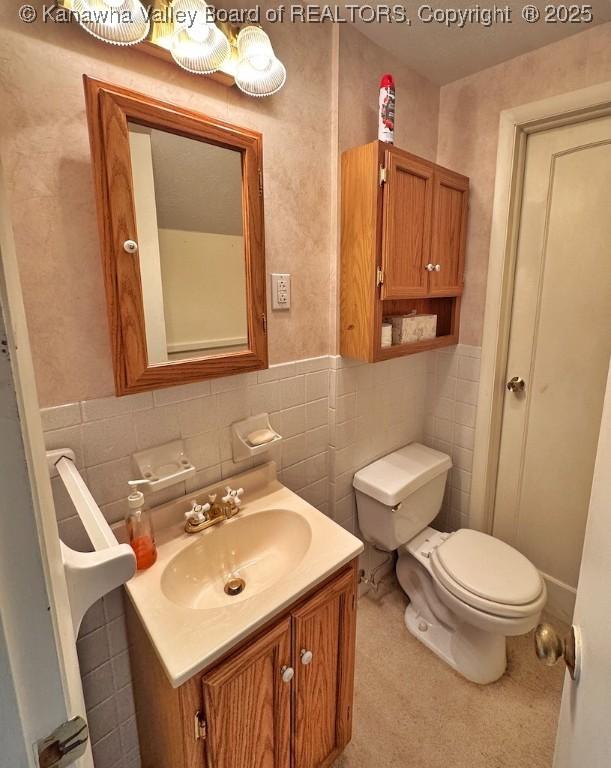 bathroom featuring a wainscoted wall, tile walls, toilet, and vanity