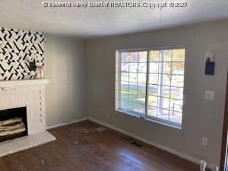 unfurnished living room with plenty of natural light, baseboards, a fireplace with raised hearth, and wood finished floors