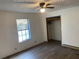 unfurnished bedroom with a baseboard heating unit, ceiling fan, a closet, and wood finished floors