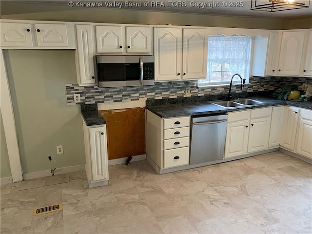 kitchen featuring a sink, appliances with stainless steel finishes, white cabinetry, dark countertops, and backsplash