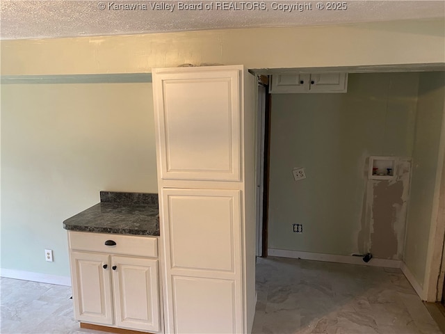 kitchen with dark countertops, white cabinets, baseboards, and a textured ceiling