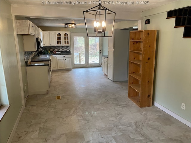 kitchen featuring baseboards, white cabinetry, dark countertops, tasteful backsplash, and a chandelier