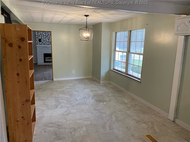 unfurnished room featuring visible vents, a notable chandelier, marble finish floor, a fireplace, and baseboards