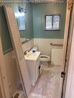 bathroom featuring tile walls, wainscoting, toilet, and vanity