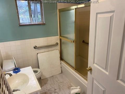 bathroom featuring tile walls, toilet, wainscoting, an enclosed shower, and vanity