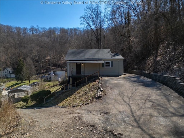 view of front of property with aphalt driveway, covered porch, and a wooded view