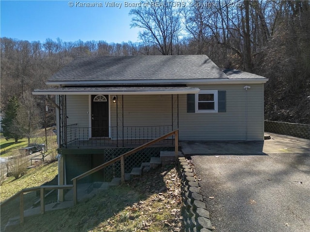 view of front facade with driveway, covered porch, a shingled roof, and stairs