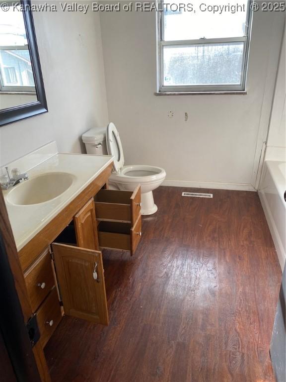 bathroom with toilet, wood finished floors, visible vents, vanity, and a bath