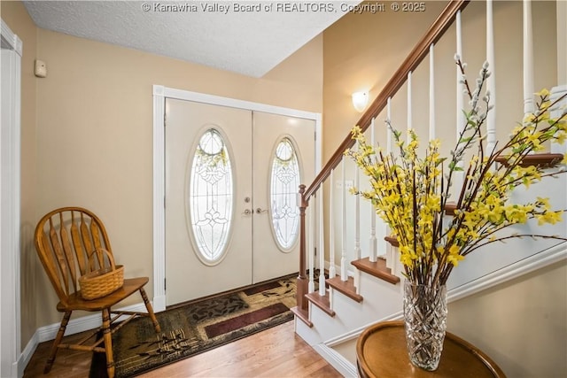 foyer featuring a textured ceiling, stairway, wood finished floors, and french doors