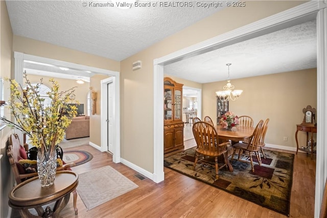 dining room featuring baseboards, visible vents, wood finished floors, an inviting chandelier, and a textured ceiling