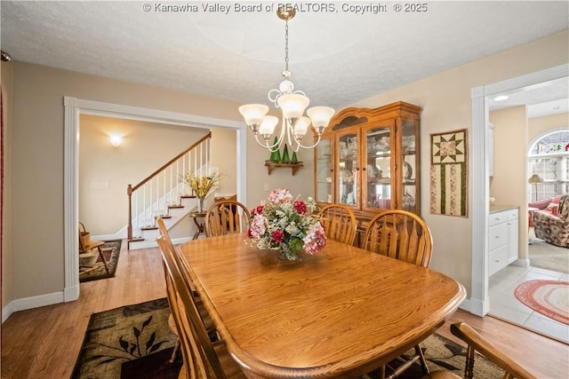 dining area featuring stairs, light wood finished floors, baseboards, and an inviting chandelier