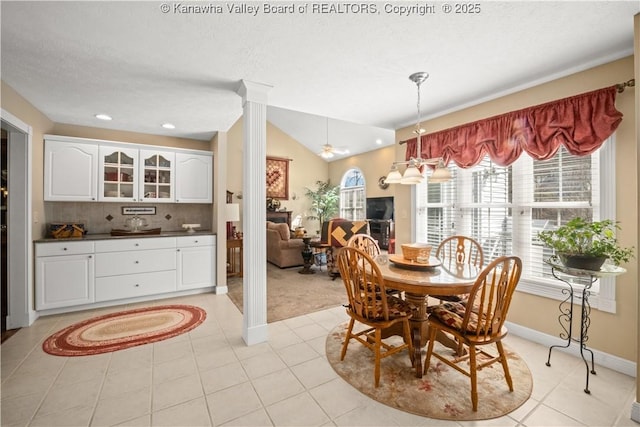 dining space with light tile patterned floors, ornate columns, vaulted ceiling, a textured ceiling, and baseboards