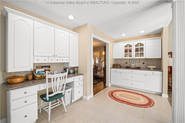 kitchen featuring built in desk, light tile patterned floors, tasteful backsplash, dark countertops, and white cabinetry