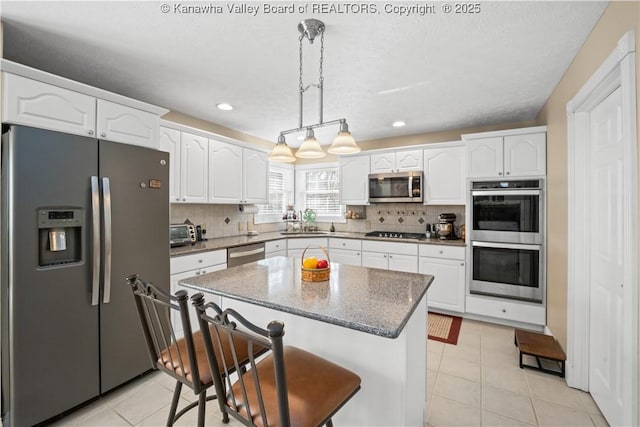 kitchen with appliances with stainless steel finishes, white cabinets, decorative backsplash, and a kitchen breakfast bar