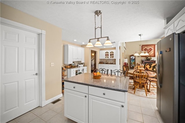 kitchen with light tile patterned floors, dark stone counters, freestanding refrigerator, and white cabinets