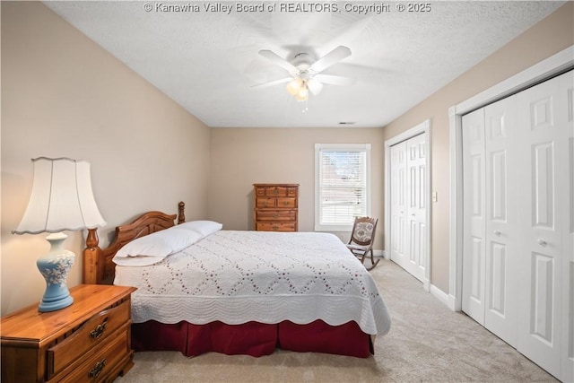 bedroom with ceiling fan, a textured ceiling, light carpet, baseboards, and two closets