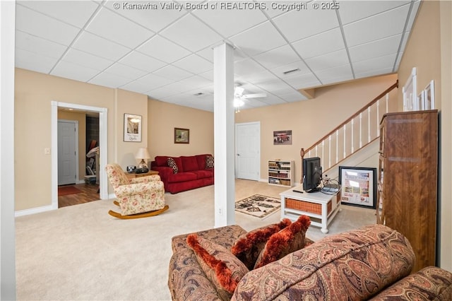 carpeted living room featuring a drop ceiling, ceiling fan, baseboards, and stairs