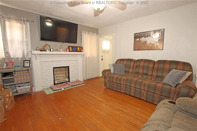 living room featuring a brick fireplace, ceiling fan, and wood finished floors