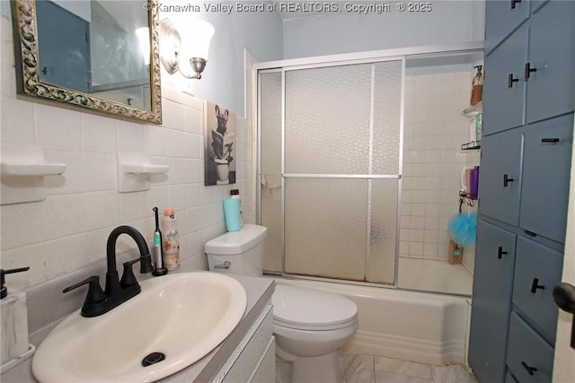 bathroom featuring toilet, a sink, marble finish floor, combined bath / shower with glass door, and tile walls