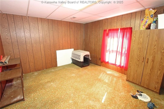 interior space with a paneled ceiling, wood walls, and carpet