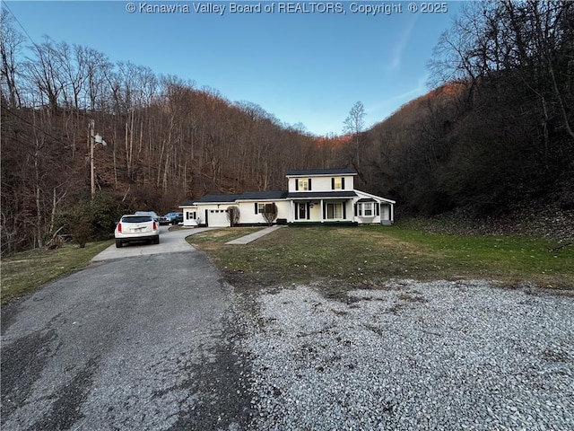 view of front of home with aphalt driveway, a front yard, a view of trees, and a garage