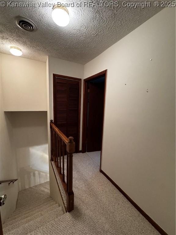 interior space with baseboards, visible vents, an upstairs landing, a textured ceiling, and carpet flooring