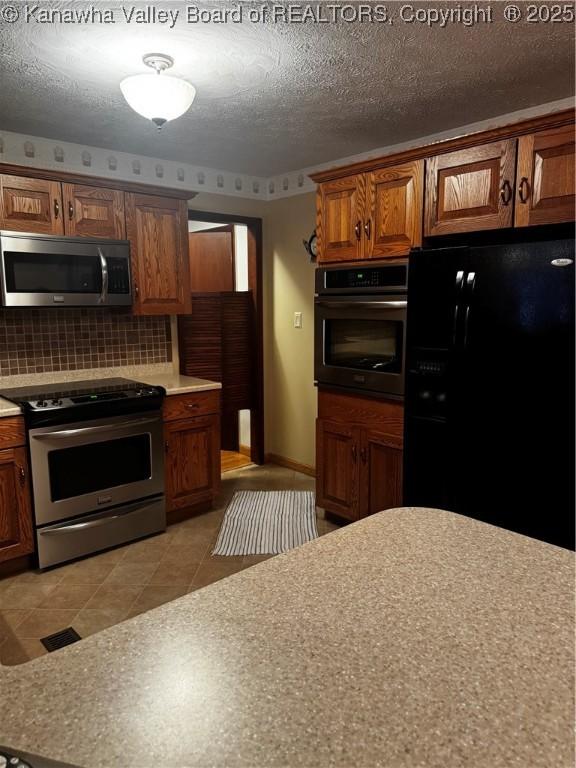 kitchen with decorative backsplash, brown cabinets, stainless steel appliances, a textured ceiling, and light countertops