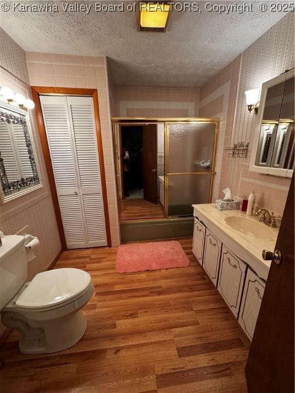 bathroom featuring a textured ceiling, toilet, wood finished floors, a shower stall, and wallpapered walls