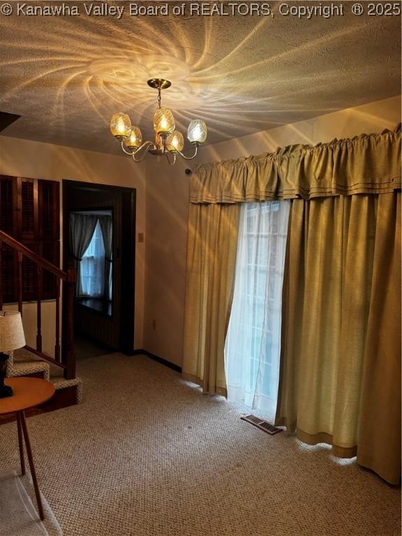 unfurnished dining area with visible vents, stairway, an inviting chandelier, a textured ceiling, and carpet floors