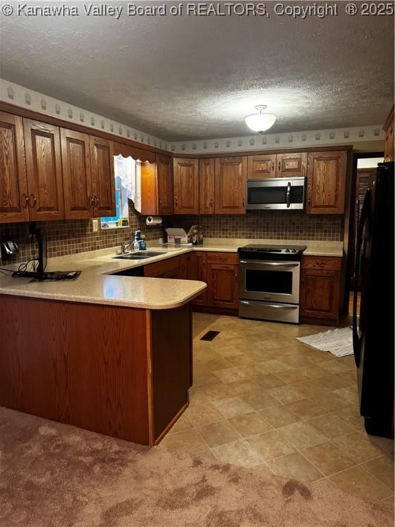 kitchen featuring stainless steel appliances, decorative backsplash, a sink, a textured ceiling, and a peninsula