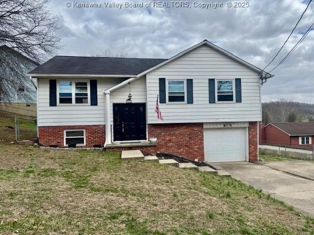 raised ranch featuring brick siding, an attached garage, fence, driveway, and a front lawn