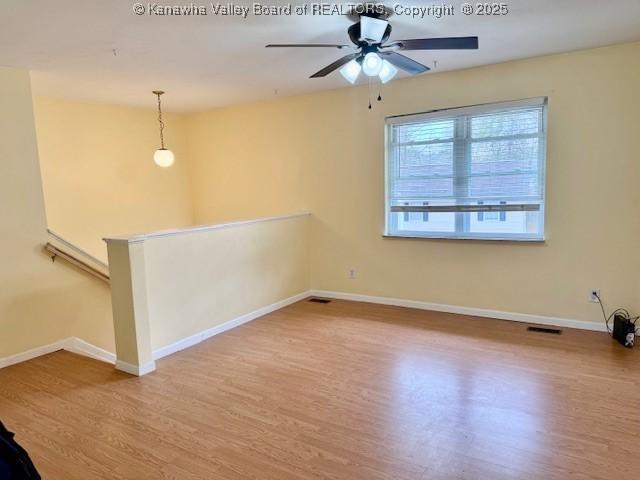 unfurnished room with a ceiling fan, visible vents, baseboards, and wood finished floors