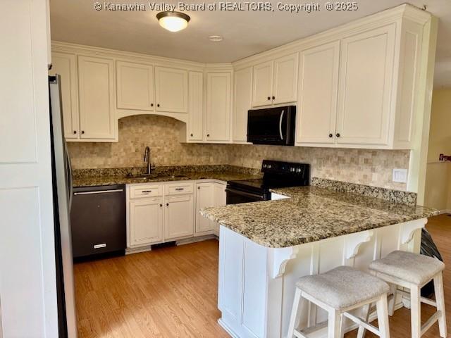 kitchen with white cabinetry, a sink, light wood-type flooring, a peninsula, and black appliances