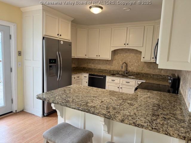 kitchen featuring dark stone countertops, a peninsula, a sink, black appliances, and backsplash