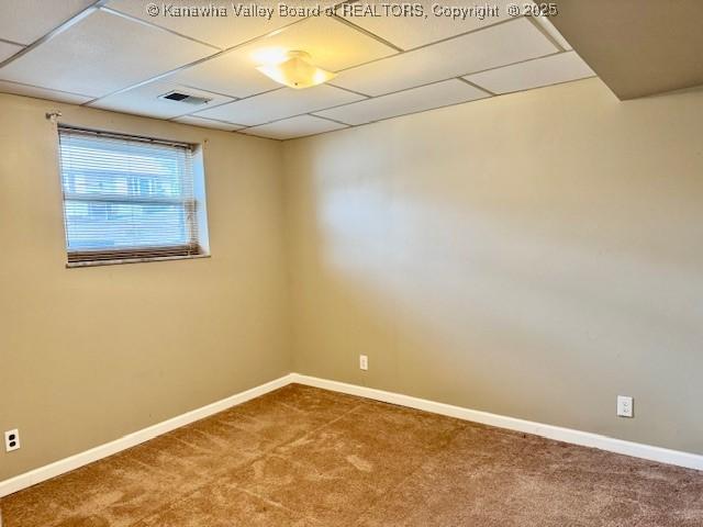 unfurnished room with visible vents, carpet flooring, a drop ceiling, and baseboards