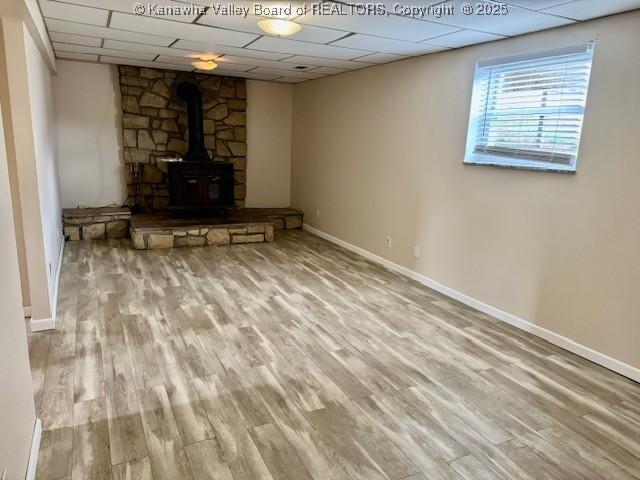 below grade area with a wood stove, a drop ceiling, and wood finished floors