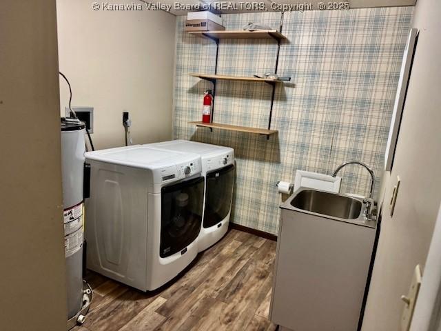 clothes washing area featuring laundry area, wood finished floors, washing machine and dryer, water heater, and a sink