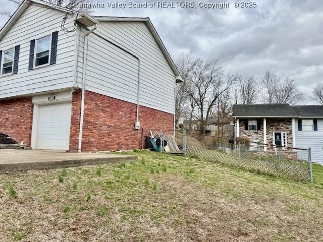 view of property exterior with a garage, fence, a lawn, and brick siding